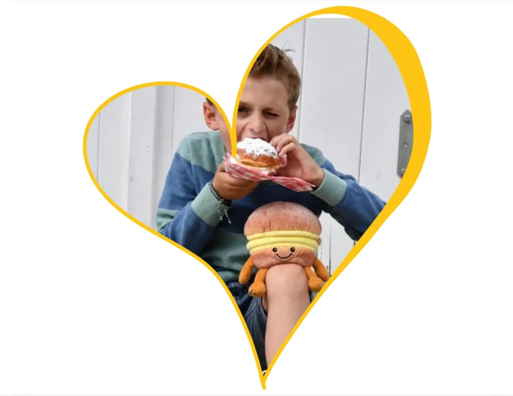 Boy eating a boule de Berlin with the custom boule de Berlin plush toy made by Progimpex for the municipality of Knokke-Heist on his knee. Photo Boy eating a boule de Berlin with the custom boule de Berlin plush toy made by Progimpex for the municipality of Knokke-Heist on his knee. Photo ©Knokke-Heist
