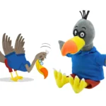 Original drawing of the bird character from publisher Kwintessens next to the plush hand puppet made by Progimpex, with the same blue shirt, red shorts, glasses and yellow beak